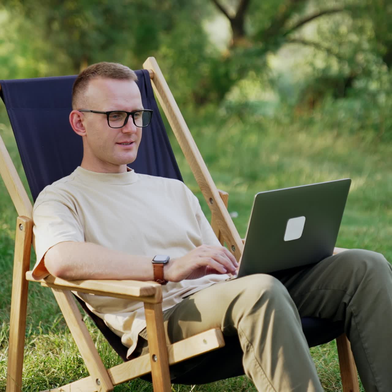 Freelancing male sits in a folding chair with laptop. Freelancer working remote in the nature