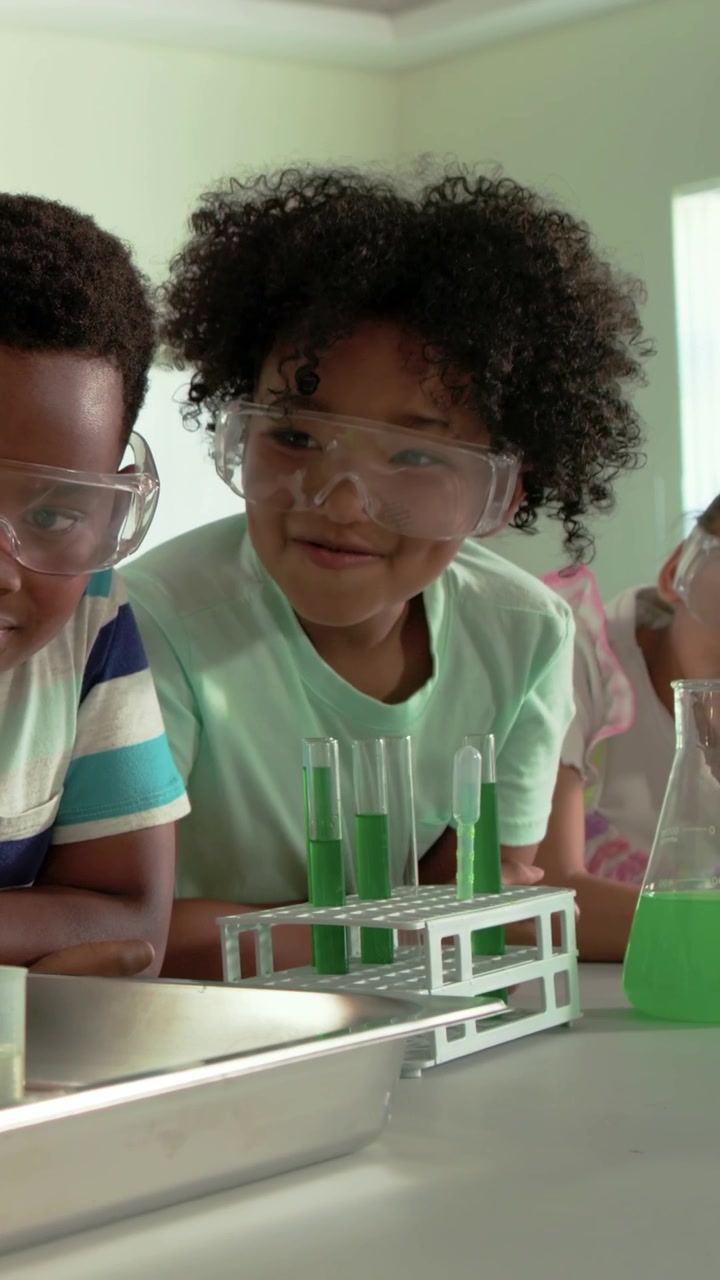 Vertical video: Students at lab table goggles on watching fizzing green tubes learning and smiling