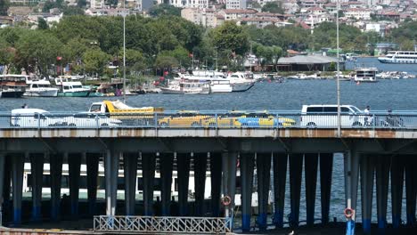 cars driving across a bridge over a harbor with boats and buildings in the background