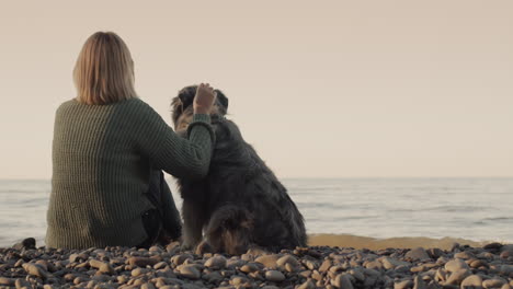 a middle-aged woman sits on the shore of the lake next to her dog, looking into the distance. rear view.