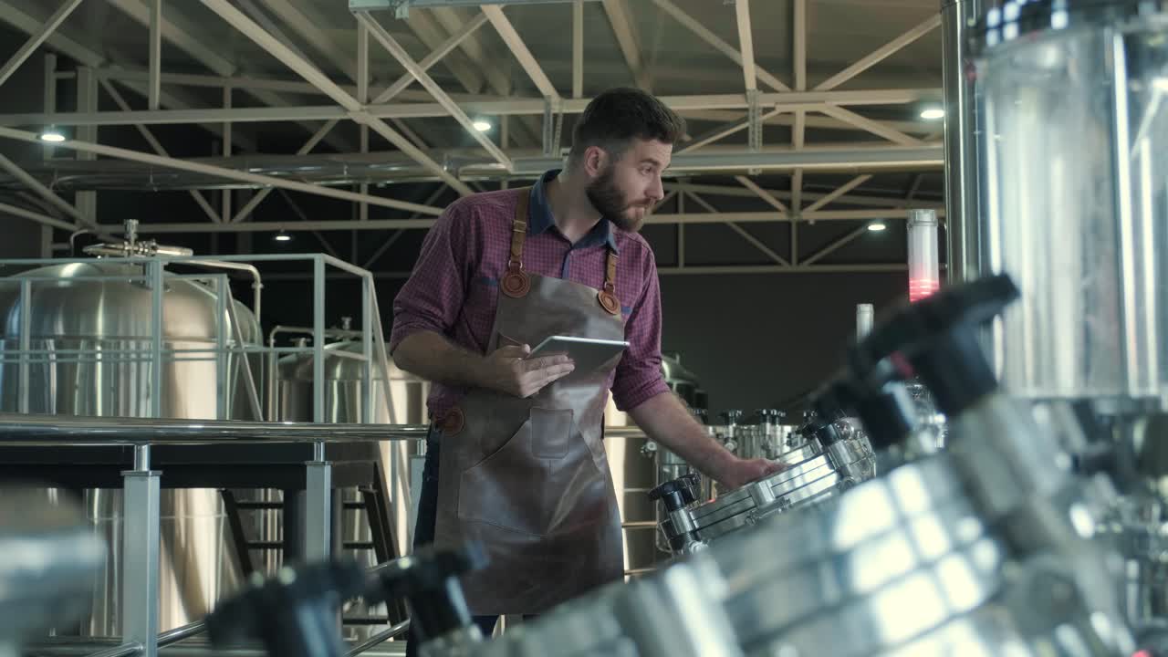 un joven cervecero con un delantal de cuero supervisa el proceso de fermentación de la cerveza en una fábrica de cerveza moderna