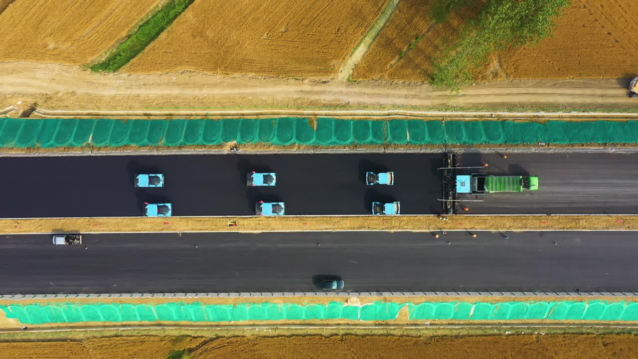 Top-down drone shot of a fleet of driverless, autonomous road rollers performing synchronized road construction in rural Bozhou, Anhui Province, China