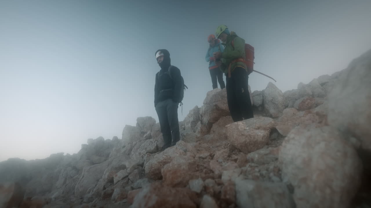 excursionistas parados en grandes rocas temprano en la mañana en el pico de la montaña triglav, mirando hacia el valle