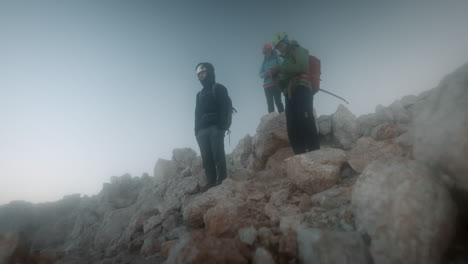 Hikers-standing-on-big-rocks-in-early-morning-on-peak-of-mountain-Triglav,-looking-into-the-valley