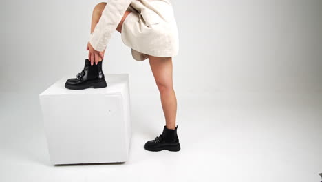woman in beige jacket and black boots on white cube