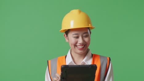 close up of asian female engineer with safety helmet working on a tablet while standing in the green screen background studio