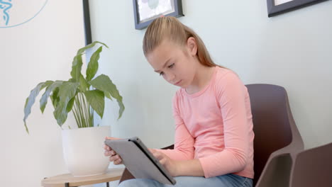 focused caucasian girl patient using tablet sitting in hospital reception, copy space, slow motion