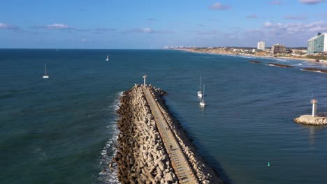 multiple sailing yachts with folded sails en route to the marina of herzeliya in israel navigating between the breakwater and the red buoy on the calm mediterranean. wide drone dolly shot
