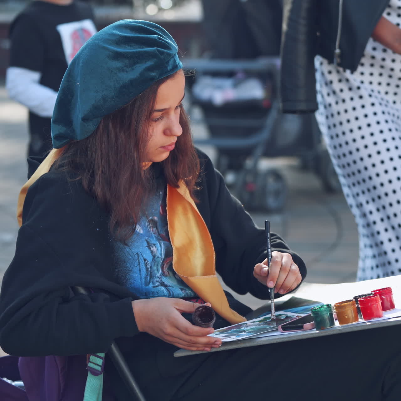 Female artist painting in the city. Young student paints picture with brush and colors on the busy street background.