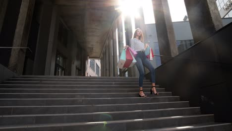 chica sonriente caminando desde el centro comercial con bolsas de compras, feliz con la compra en el viernes negro