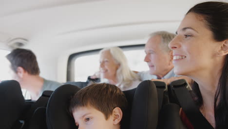 Multi-Generation-Family-Sitting-In-Back-Of-People-Carrier-Being-Driven-To-Vacation