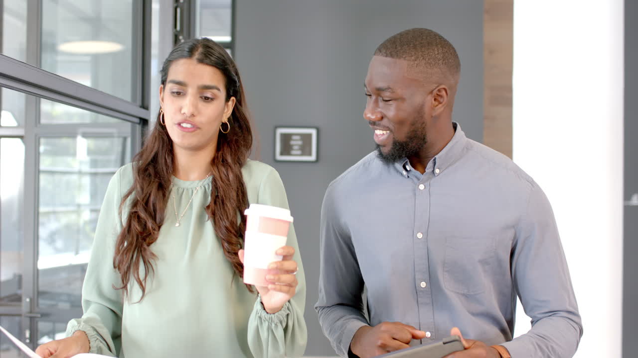 Discussing work, colleagues holding coffee cup and tablet in modern office setting