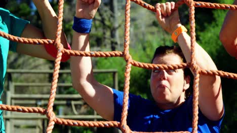 Female-trainer-assisting-women-in-climbing-net-during-obstacle-course