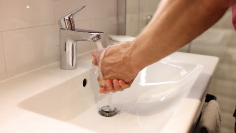 person washing hands under running water in a bathroom sink