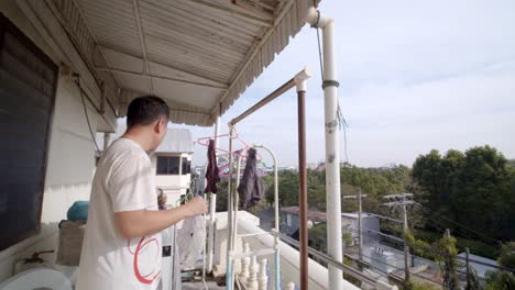 asian man out on his balcony hanging up laundry to dry in the clean fresh air - slow motion