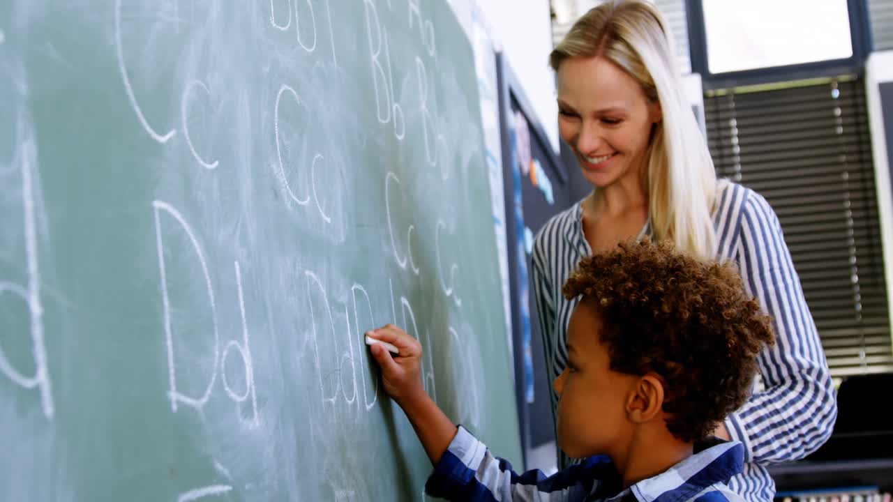 maestro ayudando a un escolar a escribir el alfabeto en la pizarra