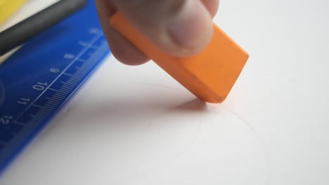 mano borrando una marca en el papel con un borrador naranja y una regla azul