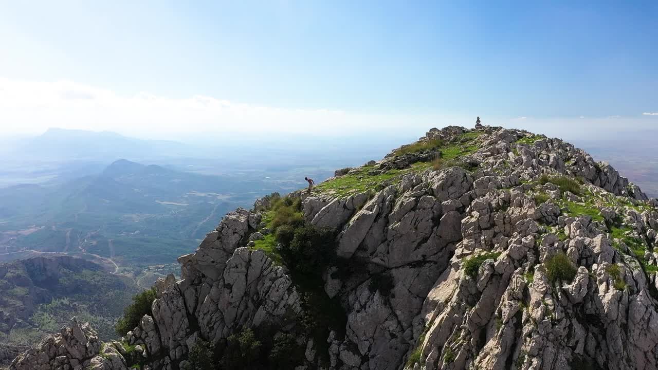un joven negro local camina por la ladera de la montaña y salta por el borde de una roca y se para en el acantilado del pico, mirando el vasto y majestuoso paisaje