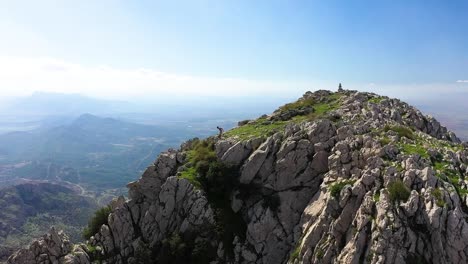 a young black local man is walking down the mountainside and jumps down the edge of a boulder and stands on the cliff of the peak, looking out over the vast and majestic landscape