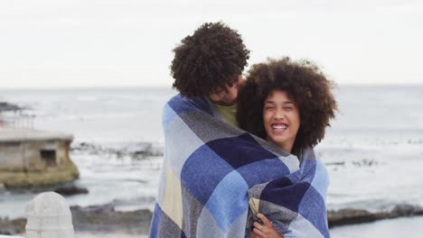 Afroamerikanisches-Paar,-Eingewickelt-In-Eine-Decke,-Lächelnd-Auf-Der-Promenade-In-Strandnähe