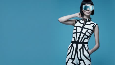 futuristic fashion shoot featuring a model in a dramatic geometric outfit and stylish reflective sunglasses against a bold blue background
