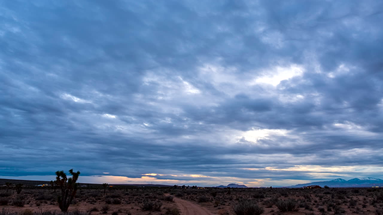 puesta de sol sobre un camino de tierra a través del paisaje del desierto de mojave con cielo nublado y montañas en la distancia - lapso de tiempo de gran angular