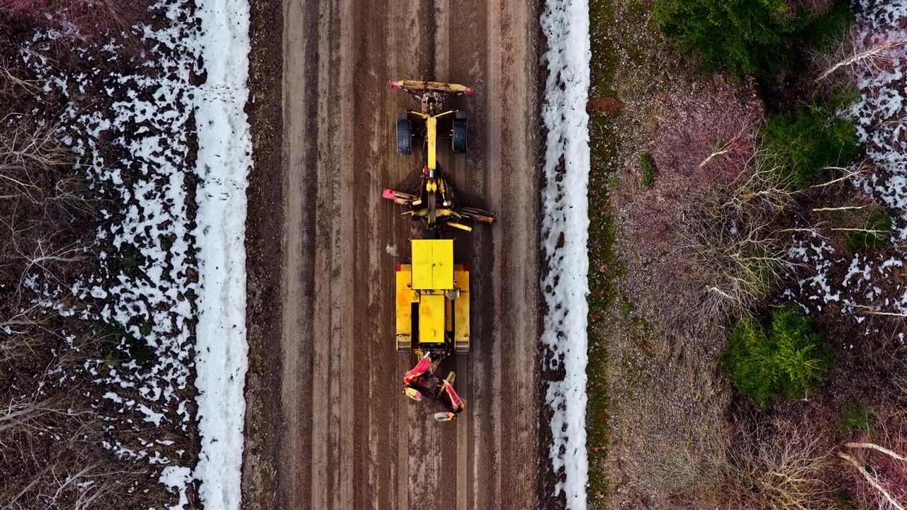 Luftfoto af tungt maskineri, der udjævner og vedligeholder en afsidesliggende landevej i det tidlige forår