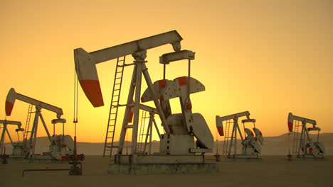 Oil-pump-jacks-pumping-oil-from-the-drilling-to-the-pipeline.-Crude-oil-is-turned-into-gasoline-and-used-as-a-source-of-energy-and-power.-Extracting-machinery-at-the-sunsetting-sky-background.