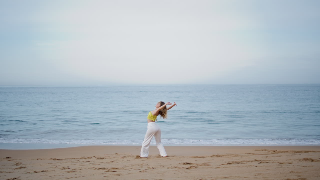 유연한 여자 댄서 몸을 구부려 저녁 해변에서 춤을 추고 있습니다.