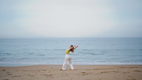 flexible girl dancer bending body performing dance on evening sea coast.