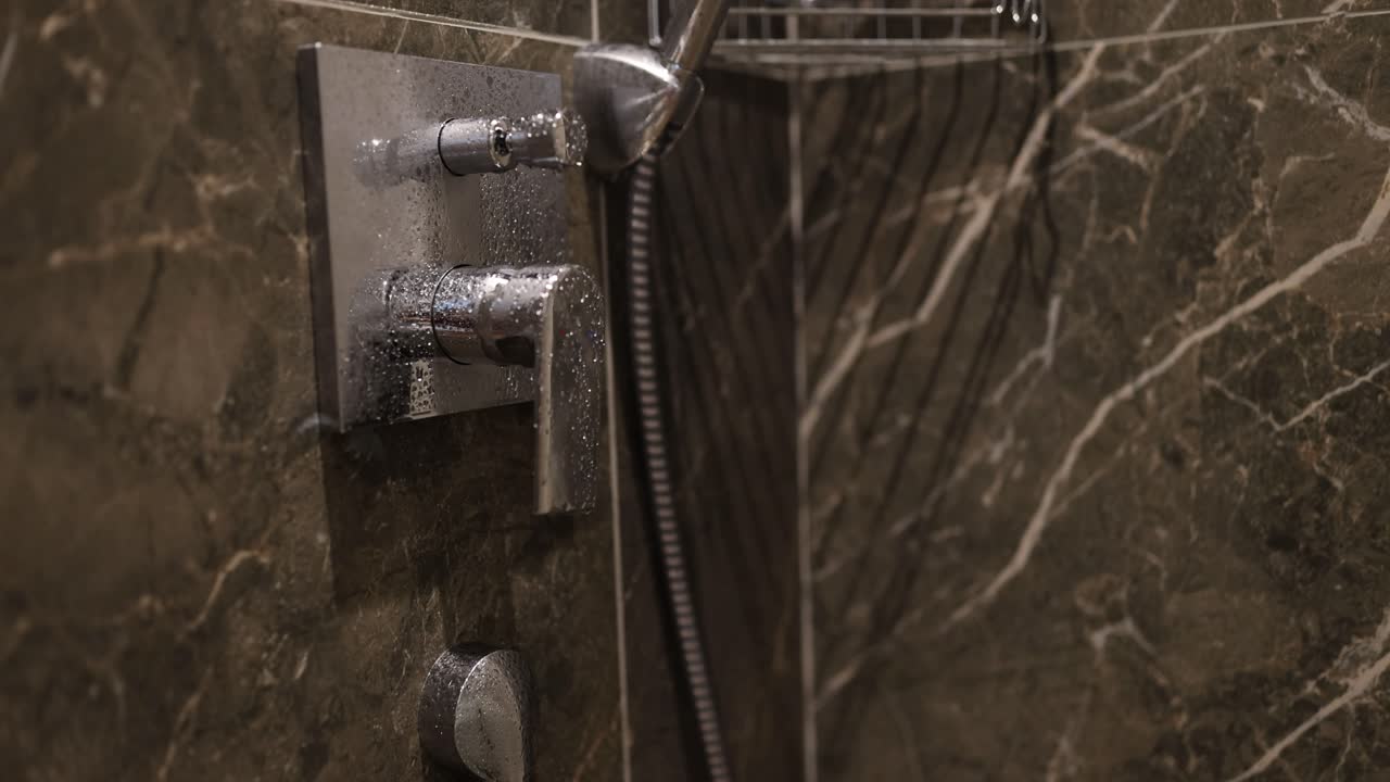 Close-up of a modern shower head and controls with water droplets on a dark marble-tiled wall