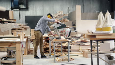 man using a chop saw in a woodworking workshop