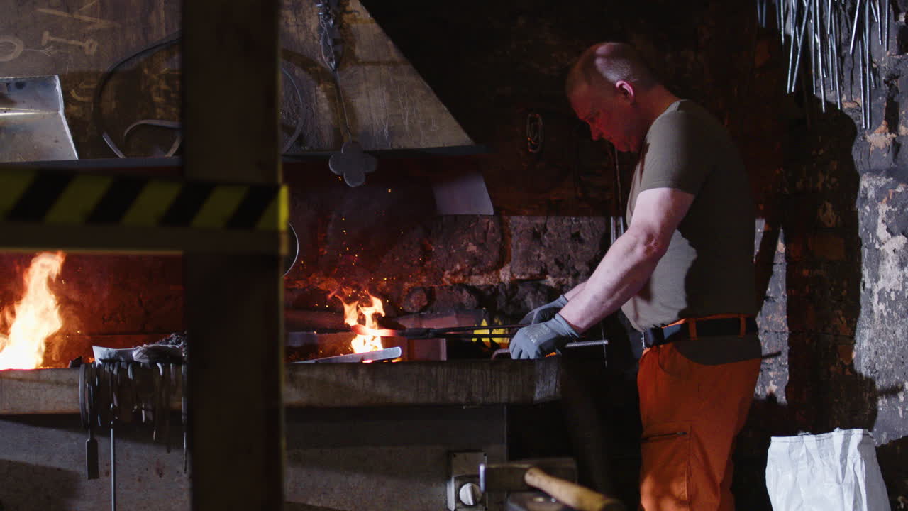 Blacksmith removes glowing red-hot piece of iron from flames in forge, slomo