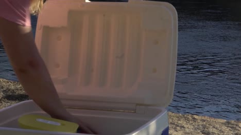 outdoor nature blonde woman looking through esky cooler box riverside camping