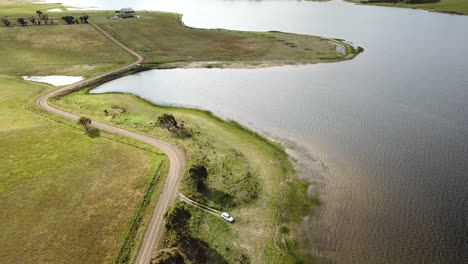 Drone-Flying-Overhead-Of-Car-And-Person-In-Isolation-Parked-Alongside-Country-Dam-in-Tasmania,-Australia