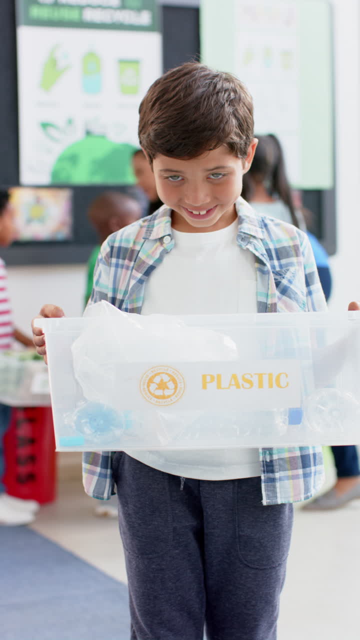 Vertical video: In school, young biracial boy holding a plastic recycling bin