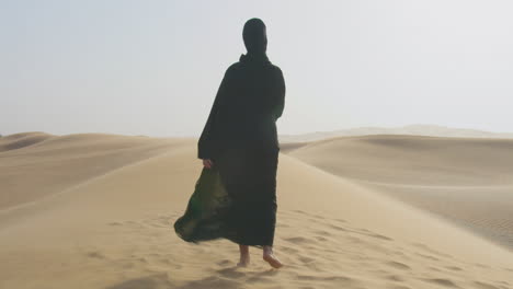 back view of a muslim woman with hijab walking barefoot in the desert 1