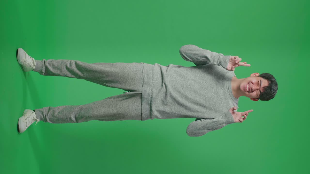 Full Body Of Smiling Asian Man Keep Fingers Crossed While Standing In Front Of Green Screen Background