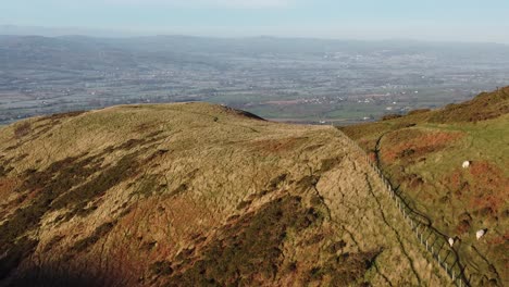 Early-sunlight-on-highland-mountain-peak-aerial-view-across-vast-frosty-idyllic-farmland-countryside-landscape-push-in