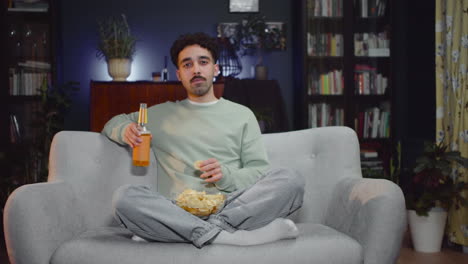 Young-Man-Watching-Comic-Movie-On-Tv-While-Eating-Chips-And-Drink-Soda-Sitting-With-Crossed-Legs-On-Couch-At-Home