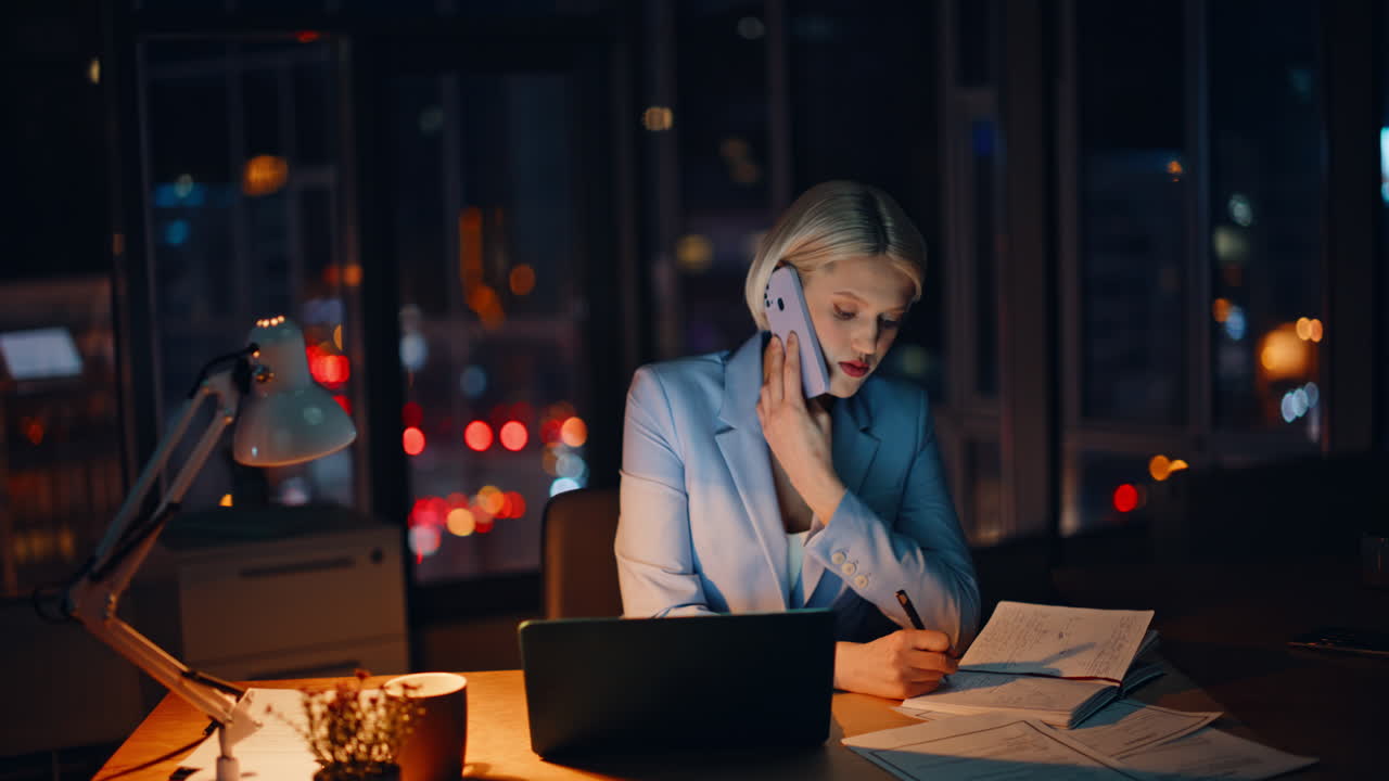 Smiling businesswoman calling late working on office laptop at evening closeup