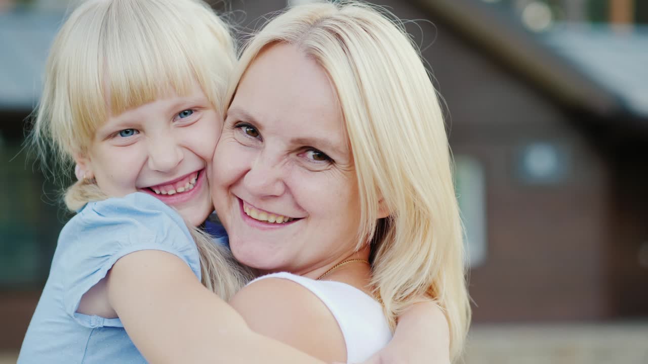 Portrait of happy mother with a little daughter hugging against the background of their new home, looking at the camera