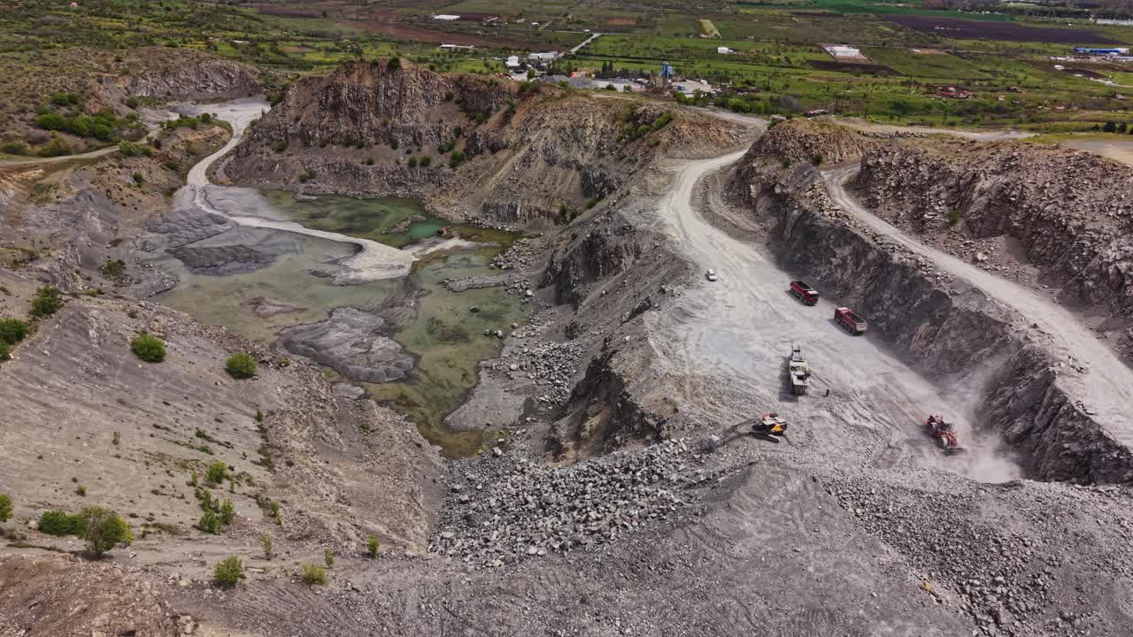 Heavy machinery works on a rocky site near a small lake in daylight