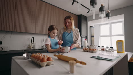 mom and little daughter are cooking together and having fun in home kitchen mother is teaching her child to cook cake