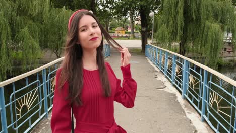 Hermosa-Morena-En-Rojo-Toca-Su-Cabello-Y-Cruza-El-Puente-En-El-Parque