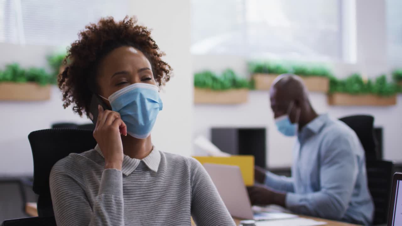 Diverse male and female business colleagues in face masks, woman talking on smartphone in office