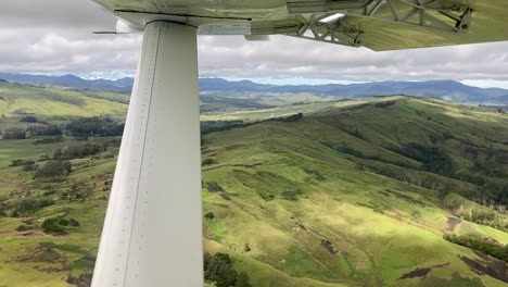 small aircraft wing dips while flying over lush green hilly landscape, aviation