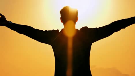 man silhouetted against sunset with arms outstretched