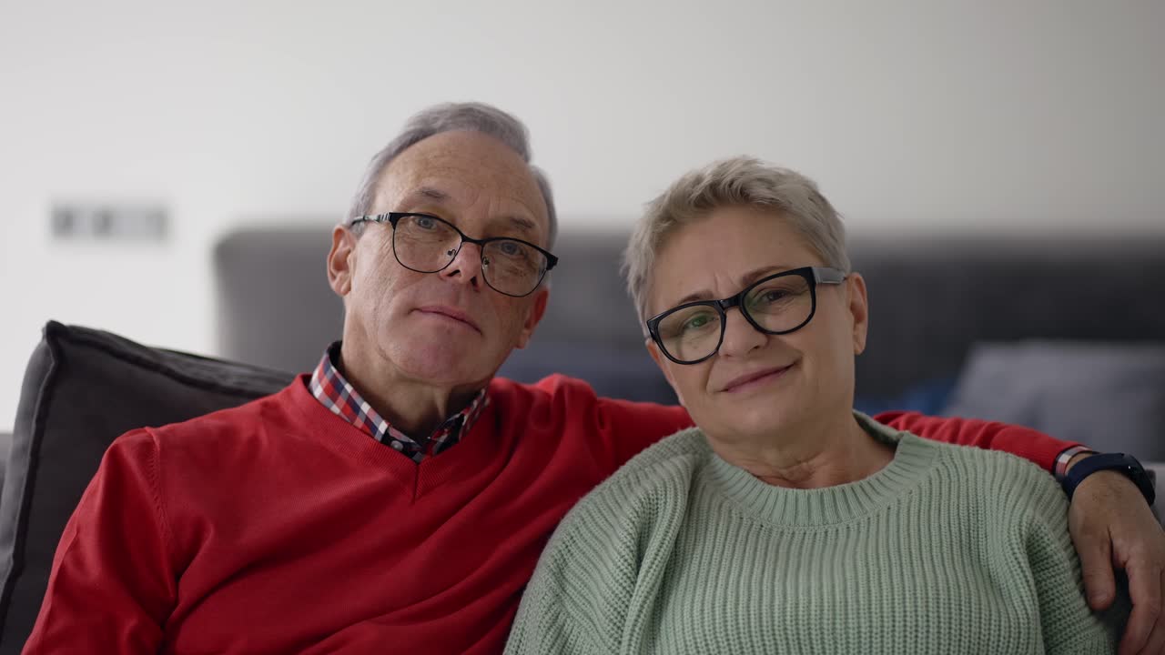 Retrato de pareja caucásica mayor sonriendo, abrazándose y sentados en el sofá.