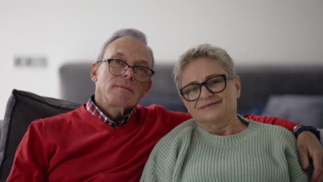 retrato de una pareja caucásica mayor sonriente abrazándose y sentada en el sofá